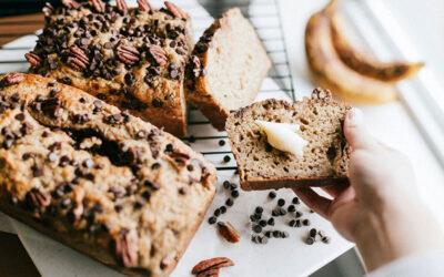 Loaves of baked bread on counter, hand holding slice with butter