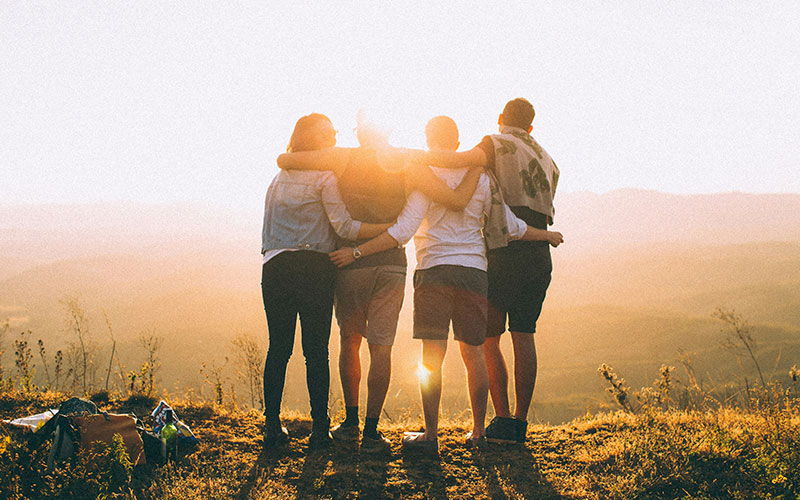 4 people together, in group hug, looking at sunrise in distance
